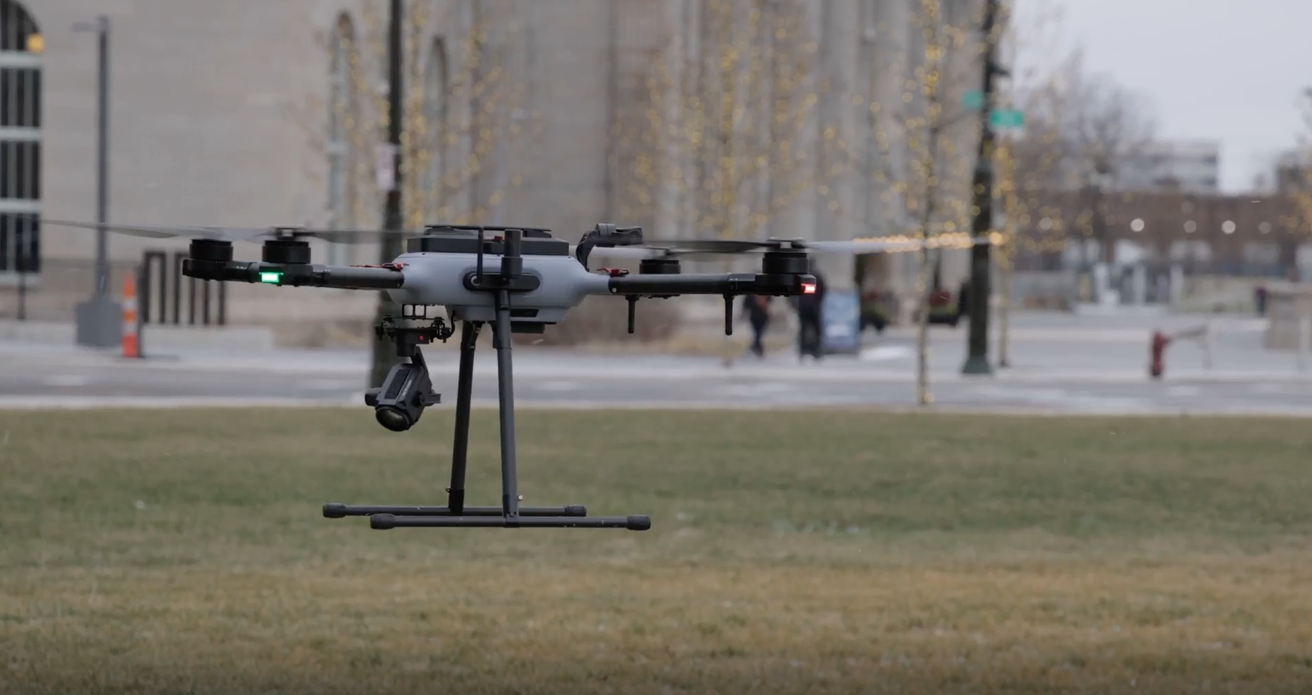 Quadcopter drone hovering low over grass with mounted camera and landing skids